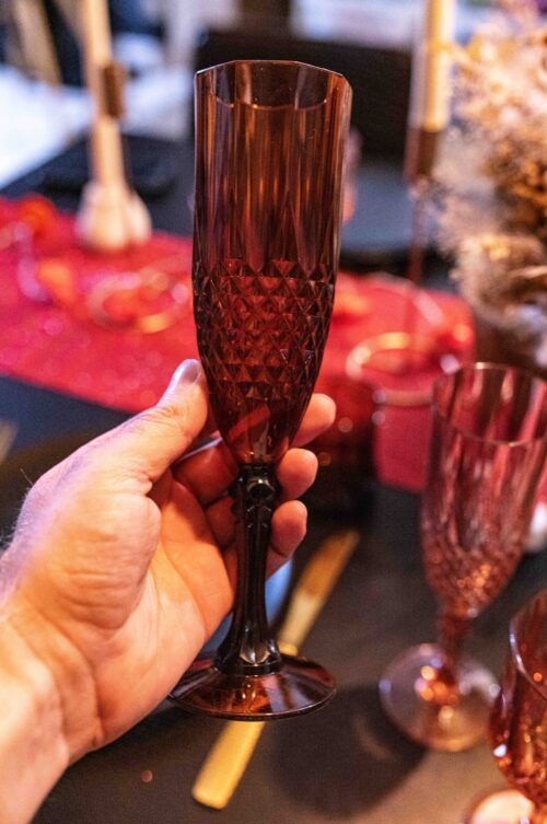 Main tenant une flûte réutilisable en plastique ambré, ambiance dîner à deux